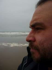 A photo of Daniel Church - a white man side-on, looking away from the camera on a beach.