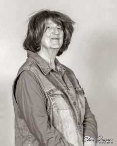 A black and white photo of Roz Kaveney - a white woman with shoulder-length brown hair, wearing a denim gillet over a long-sleeved top