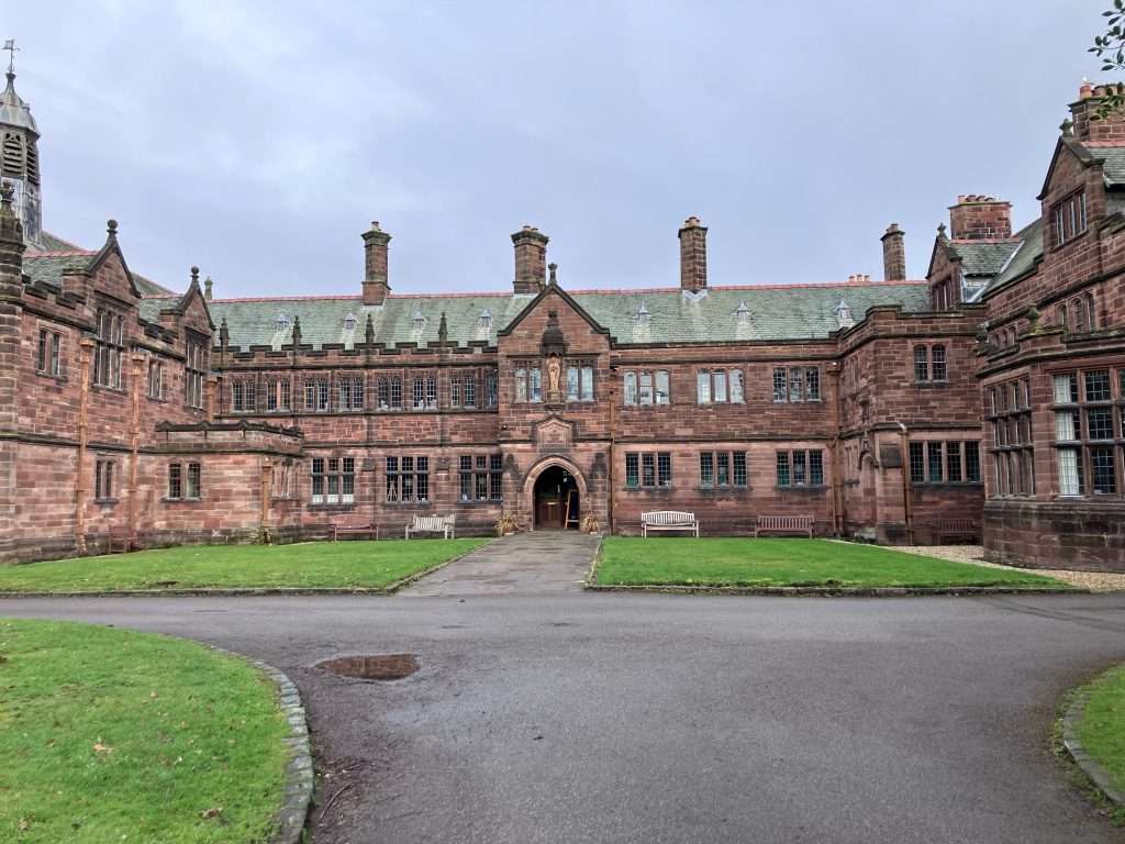 Exterior of Gladstones Library - a red sandstone building in a u-shape with a large, arched door in the centre. 