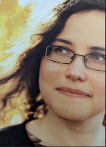 A dark haired woman wearing glasses, looking off to the side of the camera