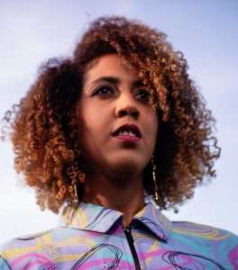 Saara El-Arifi seen from an upward camera angle. She has brown curly hair with lighter highlights and is wearing a blue and purple shirt.