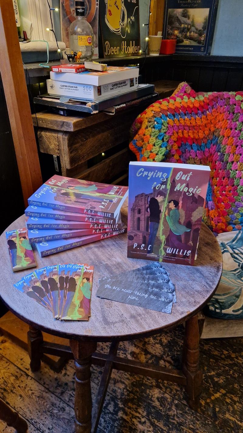 Copies of Crying Out for Magic by P.S.C. Willis on a table along with bookmarks