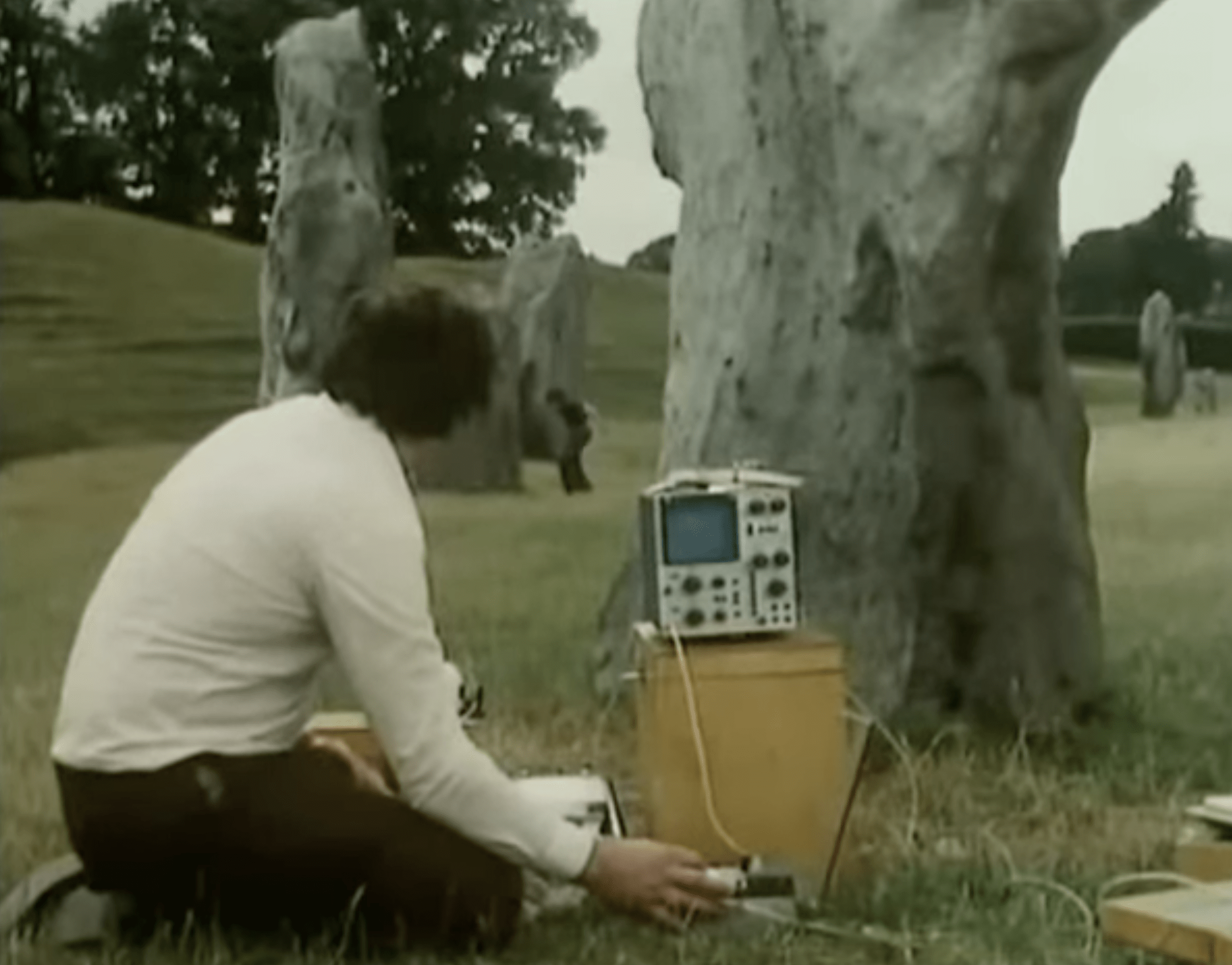 Still from the BBC TV serial Children of the Stones showing a man with scientific equipment kneeling in front of a stone circle