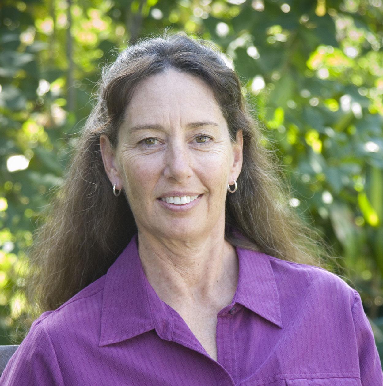 L.D. Colter smiles at the camera. She wears a purple shirt and has long brown hair.