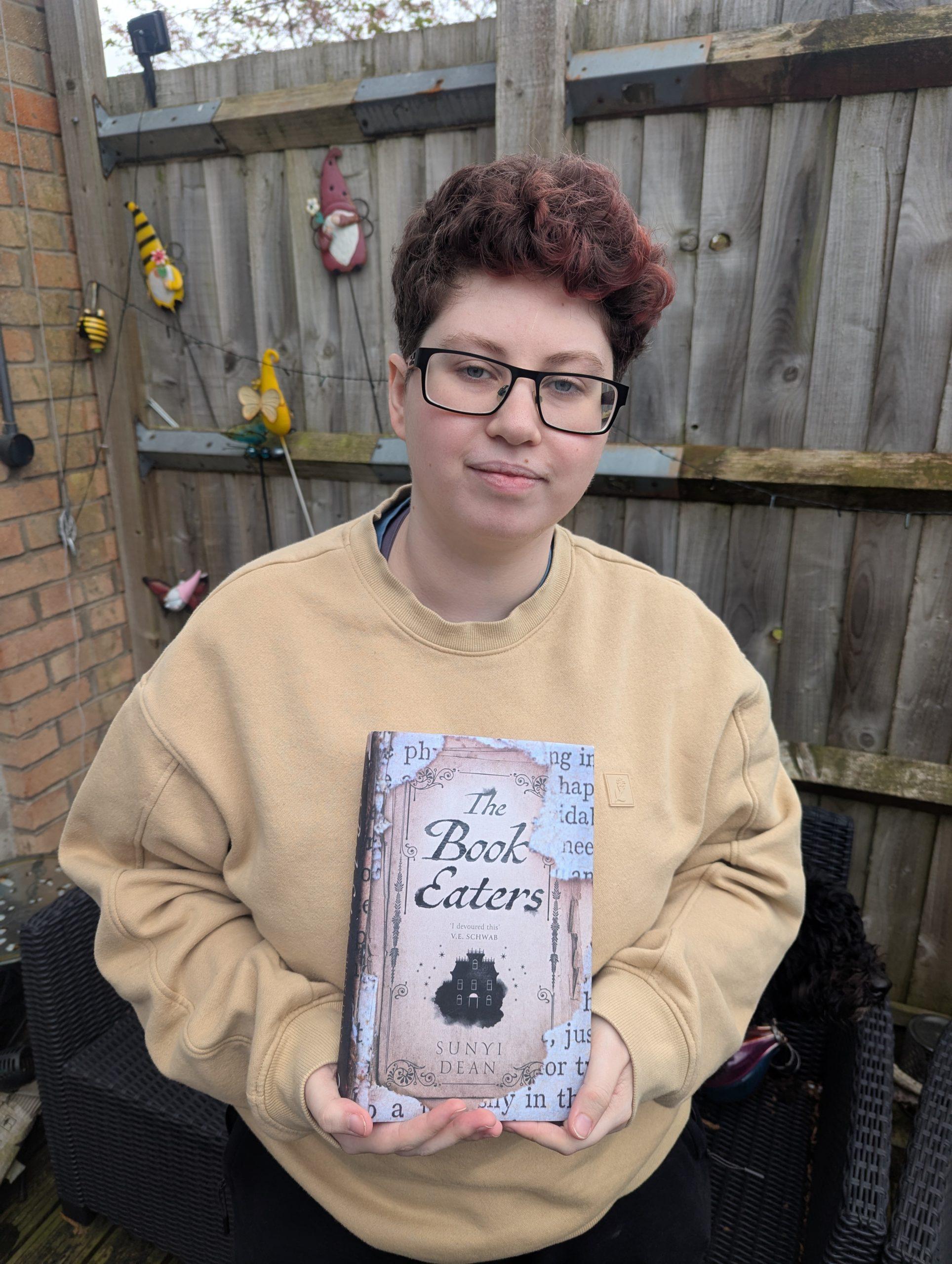 Han Noss holding Book Eaters by Sunyi Dean (their first ever intentionally-bought signed hardback)