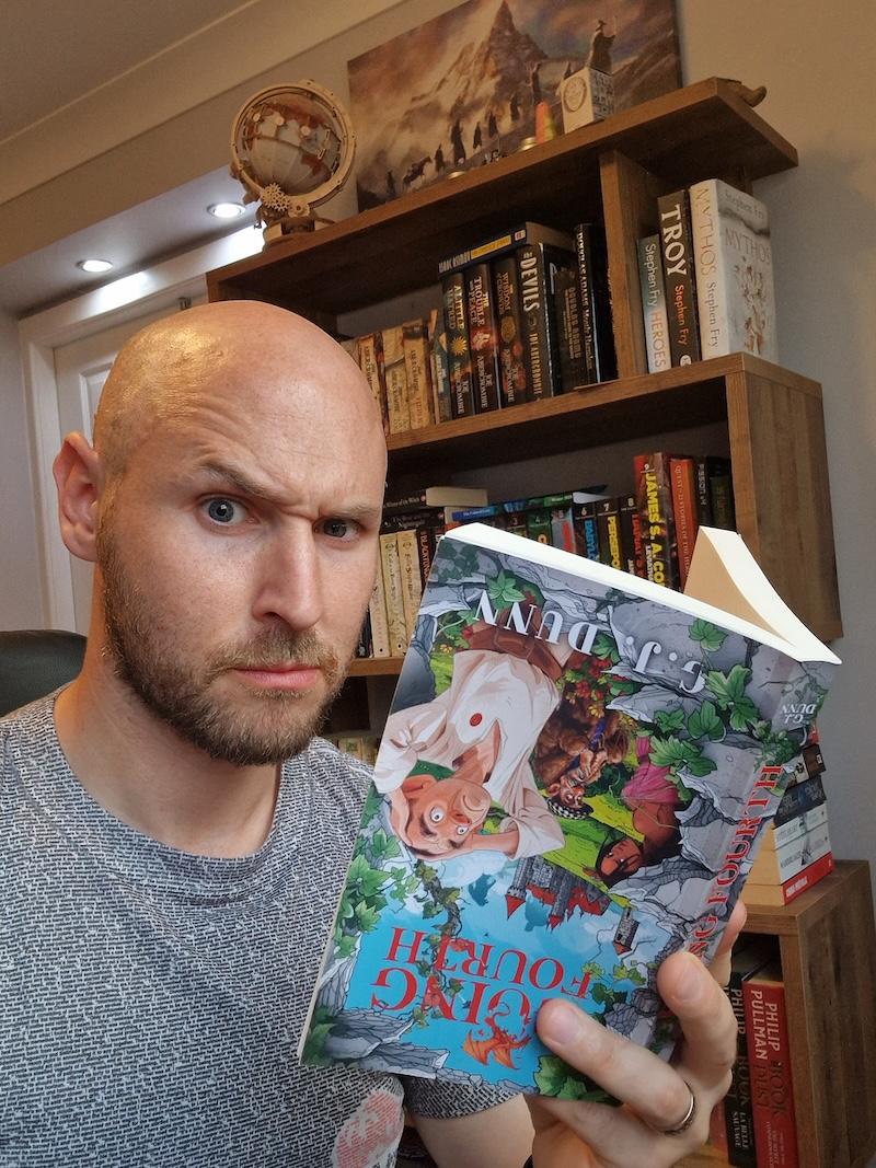 Author GJ Dunn holds a copy of his own book upside down while raising an eyebrow to the camera