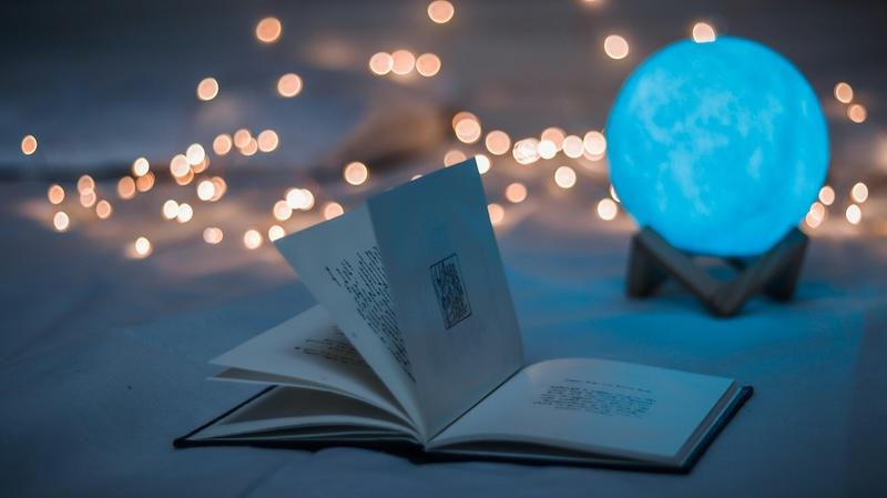 A blue glowing crystal ball sits in front of fairy lights, and behind an open book