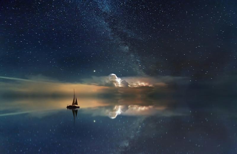 A boat sails on a flat water, with the stars and clouds reflected