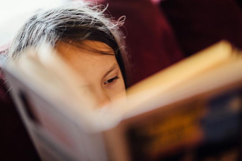 A young girl is reading, barely visible behind the book
