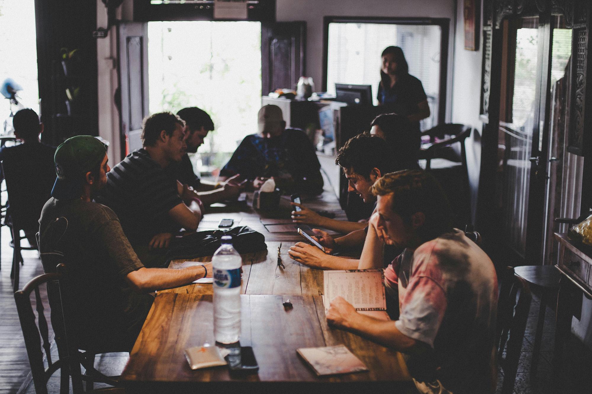 A group of people sitting in a coffee shop with books and tablets, talking to each other