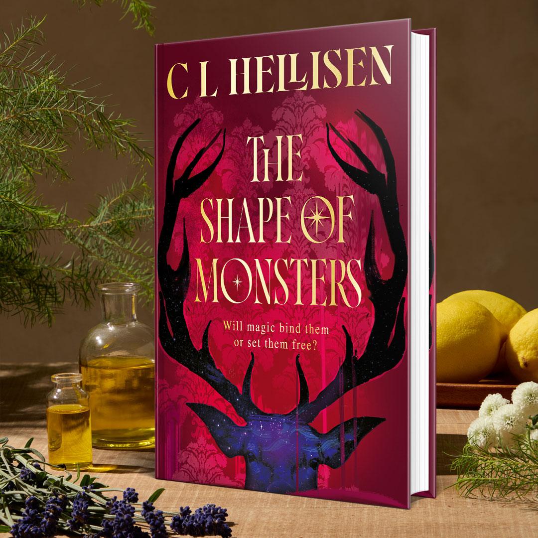 The book The Shape of Monsters by CL Hellisen sits on a table surrounded by herbs, oils and lemons