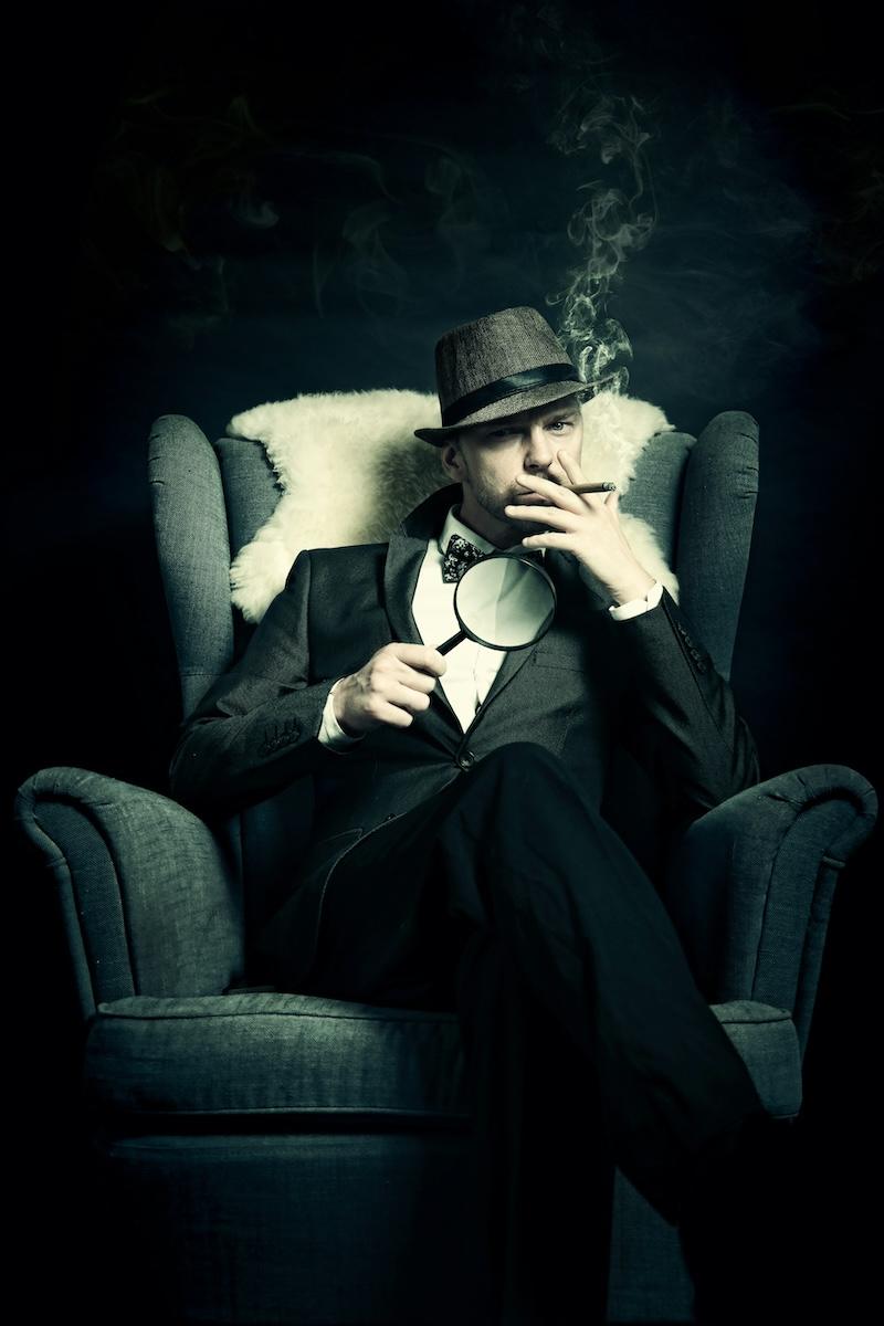 A man sitting in an armchair with a magnifying glass, smoking a cigar