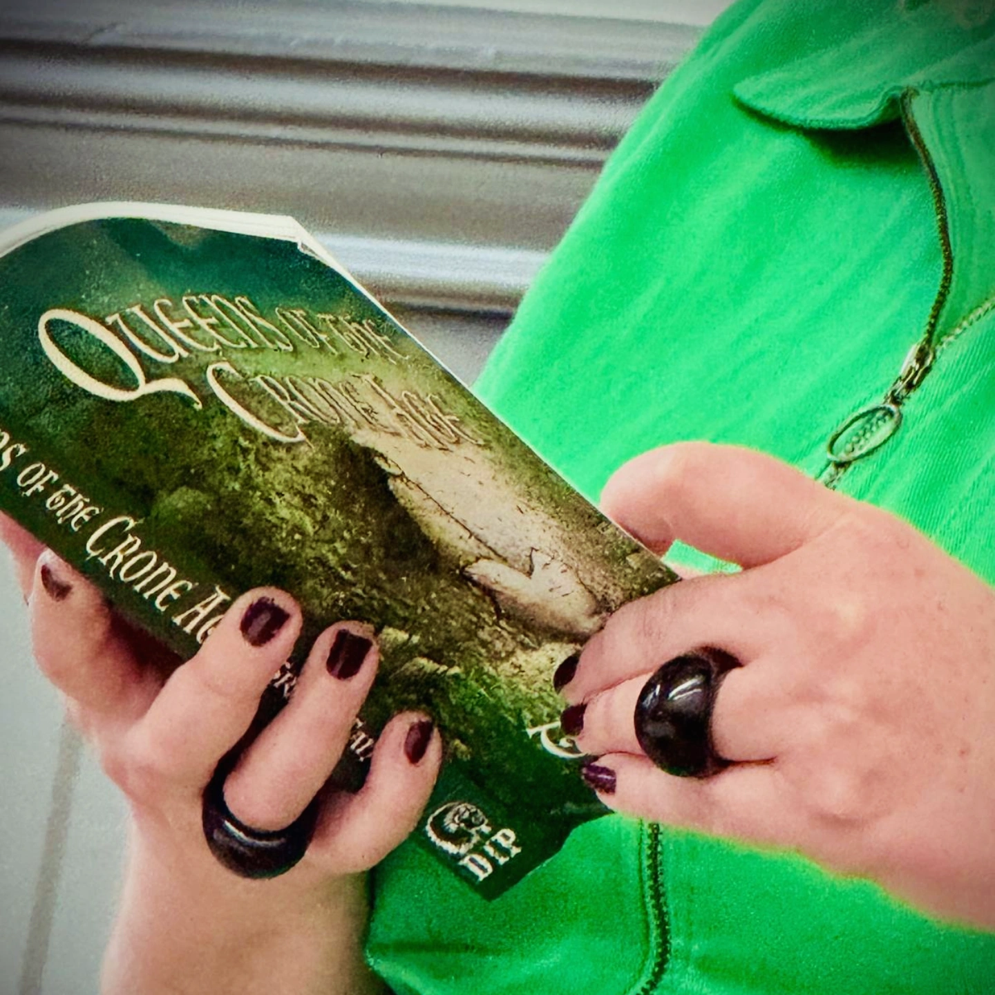 A woman in green reads Queens of the Crone Age by Tracy Fahey